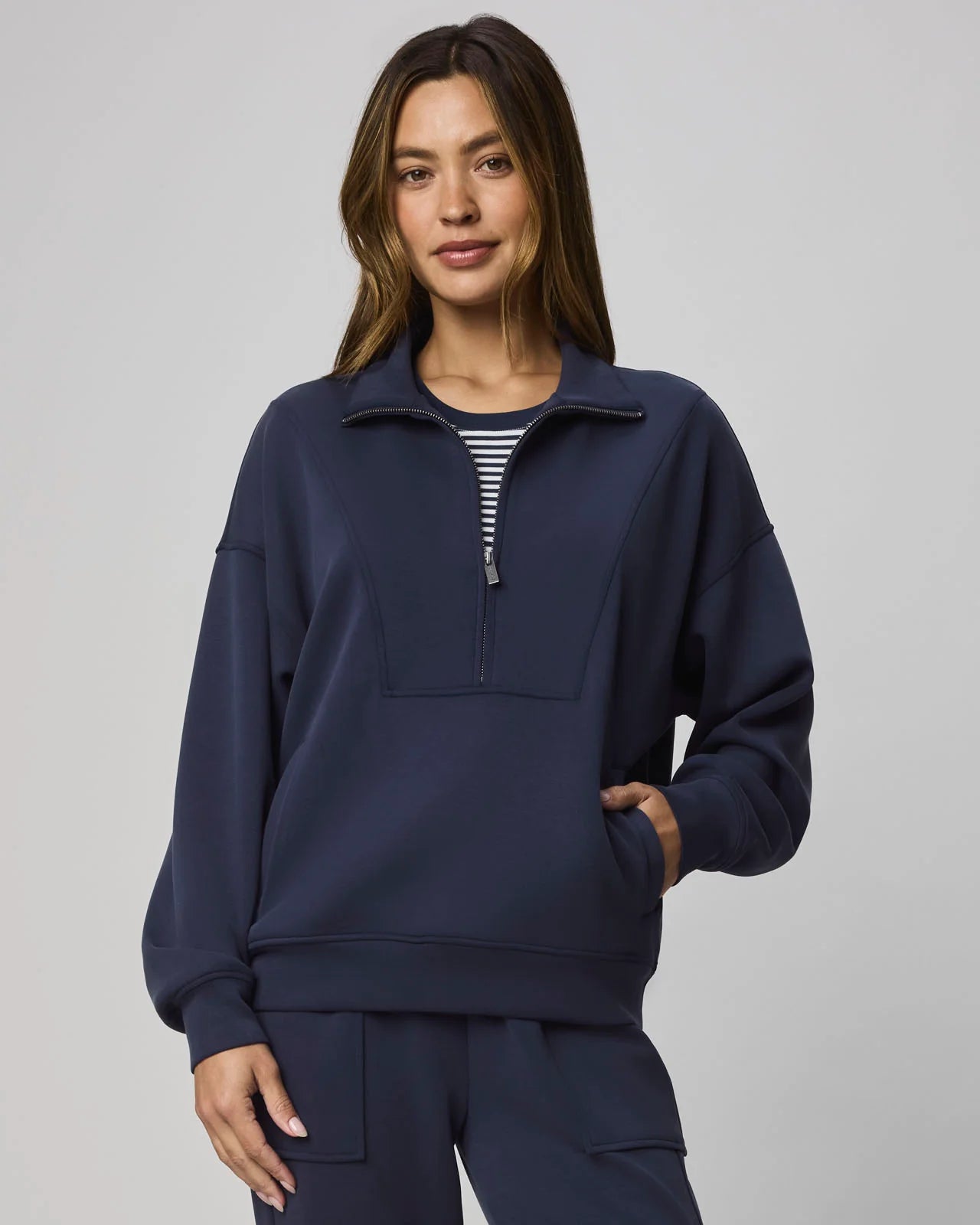 Woman wearing a navy blue pullover with a zipper on a gray background