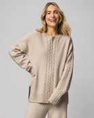Woman wearing a beige cable knit sweater on a plain background
