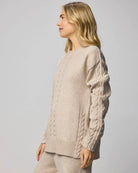 Woman wearing a beige cable knit sweater against a plain background