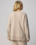 Woman wearing a beige sweater with cable knit pattern on a plain background