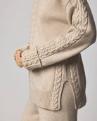 Beige cable knit sweater with detailed arm design on a light gray background