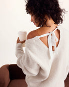 Woman wearing a white sweater with a bow detail, holding a coffee cup.