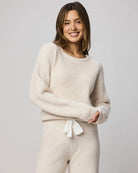 Woman wearing a beige sweater and pants set on a plain background