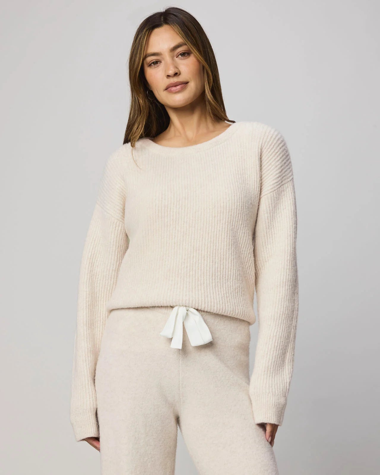 Woman wearing a beige sweater and pants set against a plain background