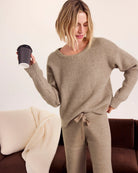 Woman in beige lounge set holding a black cup on a couch with a white blanket.