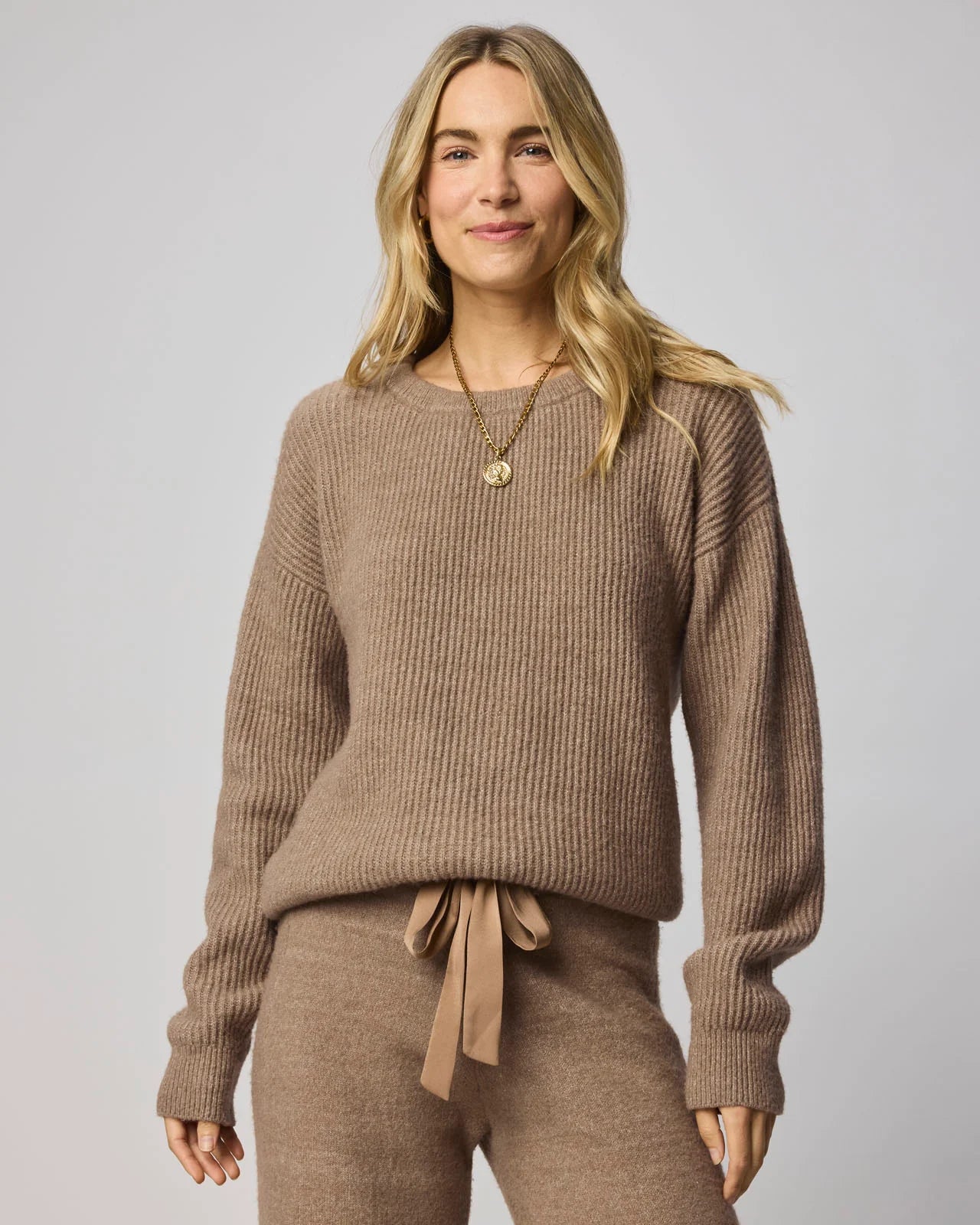Woman wearing a brown ribbed sweater and pants on a plain background