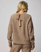 Woman wearing a brown sweater with a bow detail on the back against a plain background