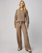 Woman wearing a brown knit outfit with a sweater and pants on a plain background