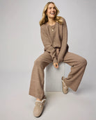 Woman wearing a brown outfit sitting on a box against a plain background