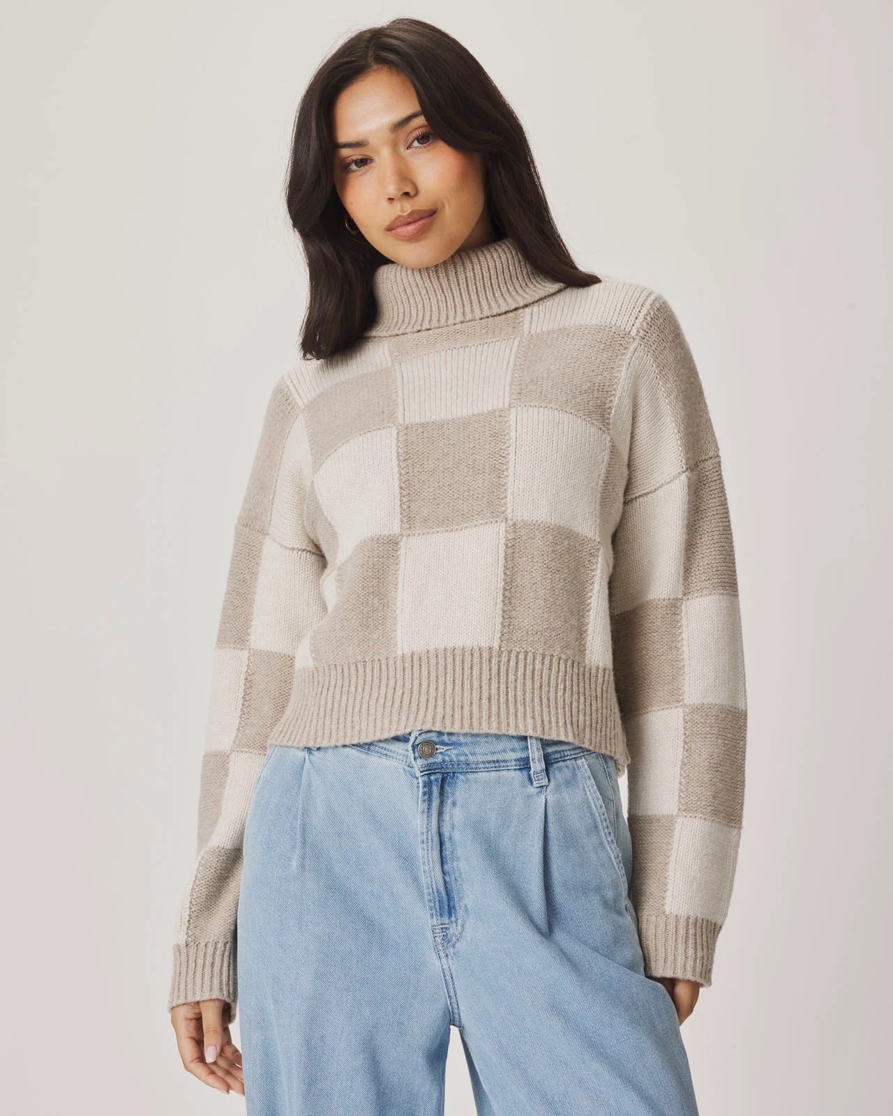 Woman wearing a checkered sweater and blue jeans against a plain background