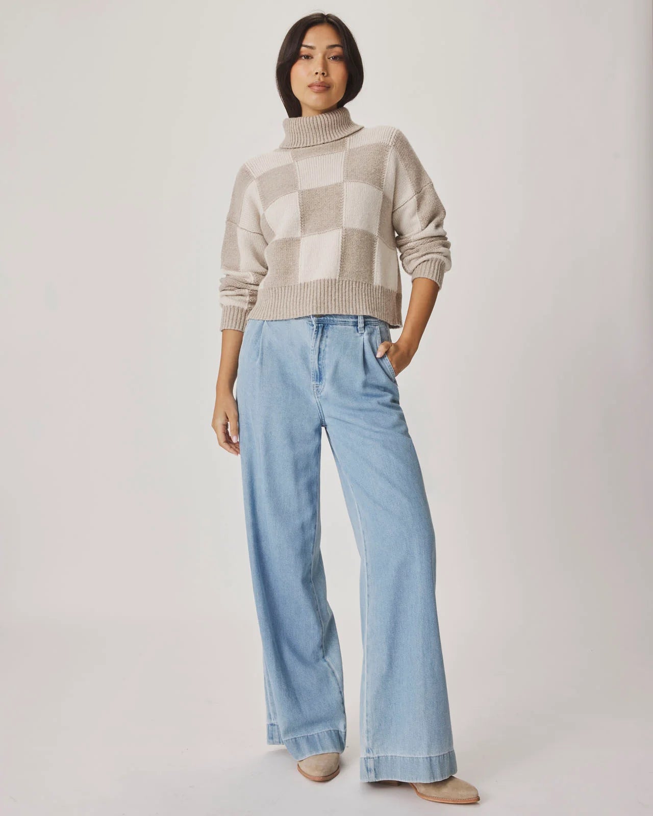 Person wearing a checkered sweater and light blue jeans on a plain background