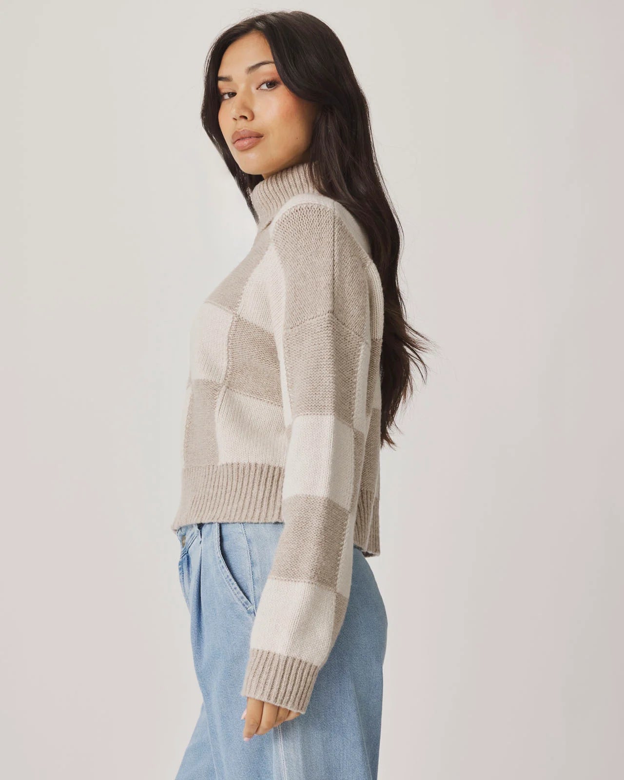 Woman wearing a plaid sweater and light blue jeans against a white background