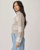 Woman wearing a plaid sweater and light blue jeans against a white background