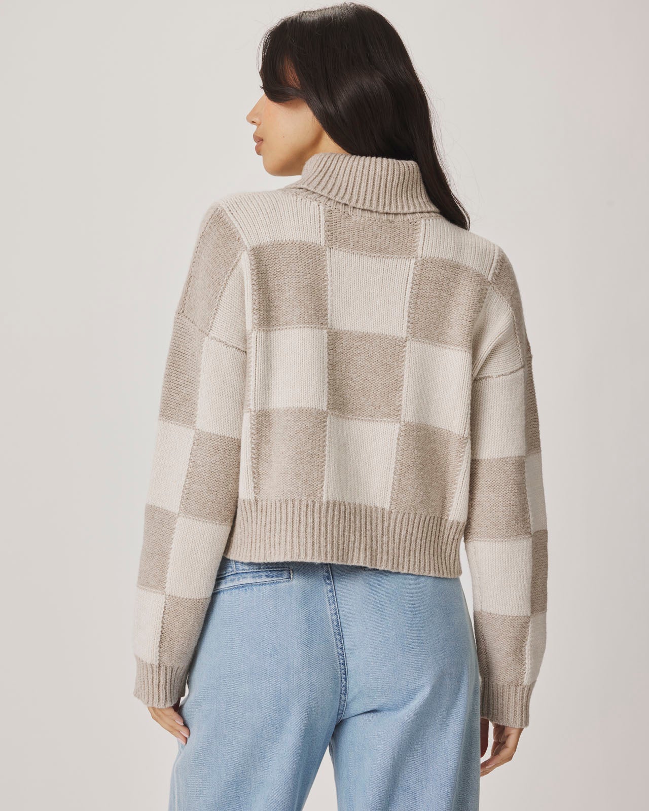 Woman wearing a checkered sweater and light blue jeans against a plain background