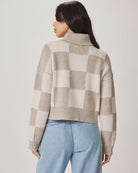 Woman wearing a checkered sweater and light blue jeans against a plain background