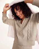 Woman wearing a beige cable knit sweater with a hood on a white background