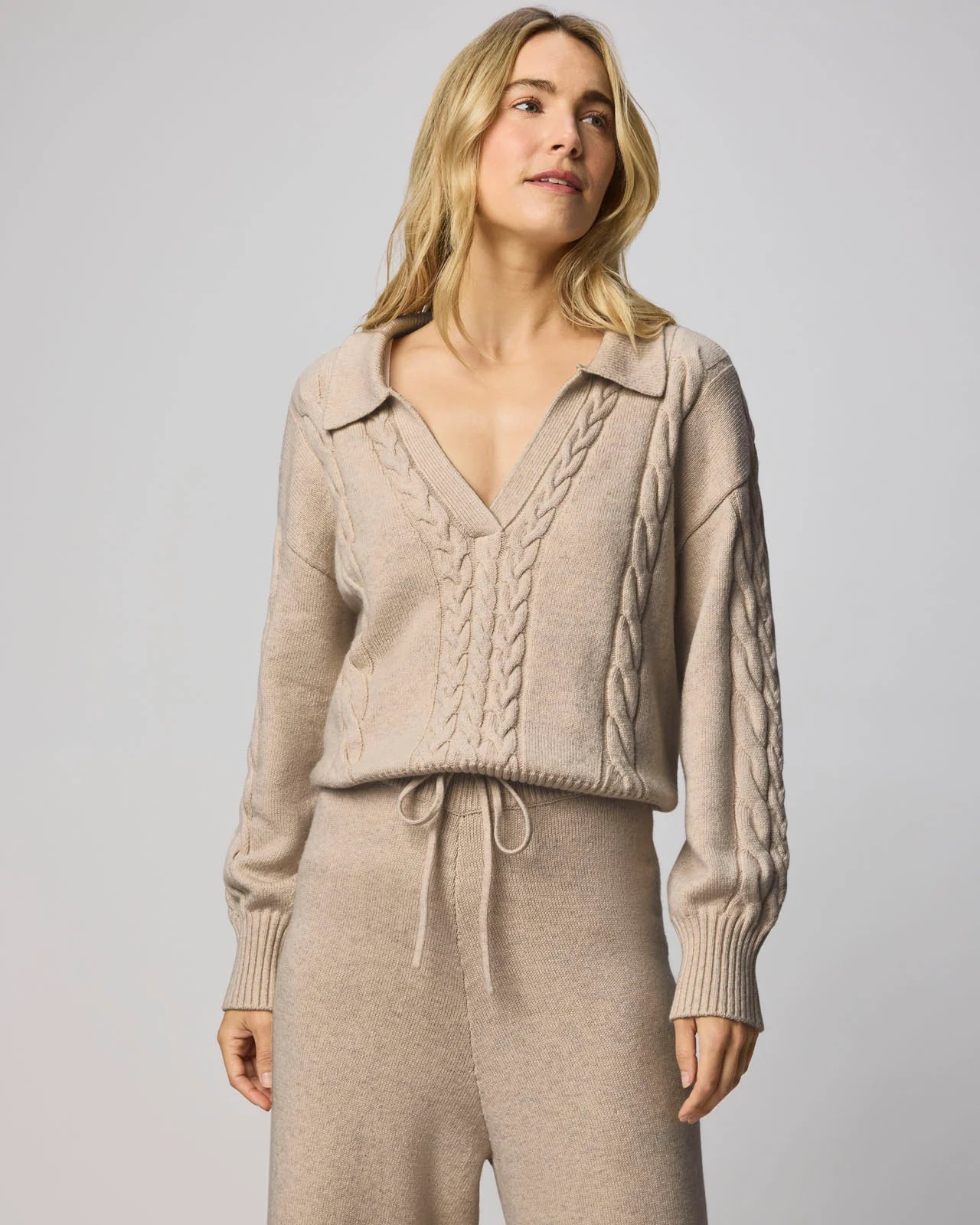 Woman wearing a beige knit outfit against a plain background