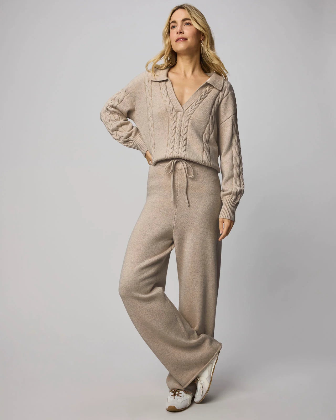 Woman wearing a beige knit sweater and pants set on a gray background