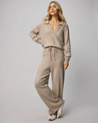 Woman wearing a beige knit sweater and pants set on a gray background