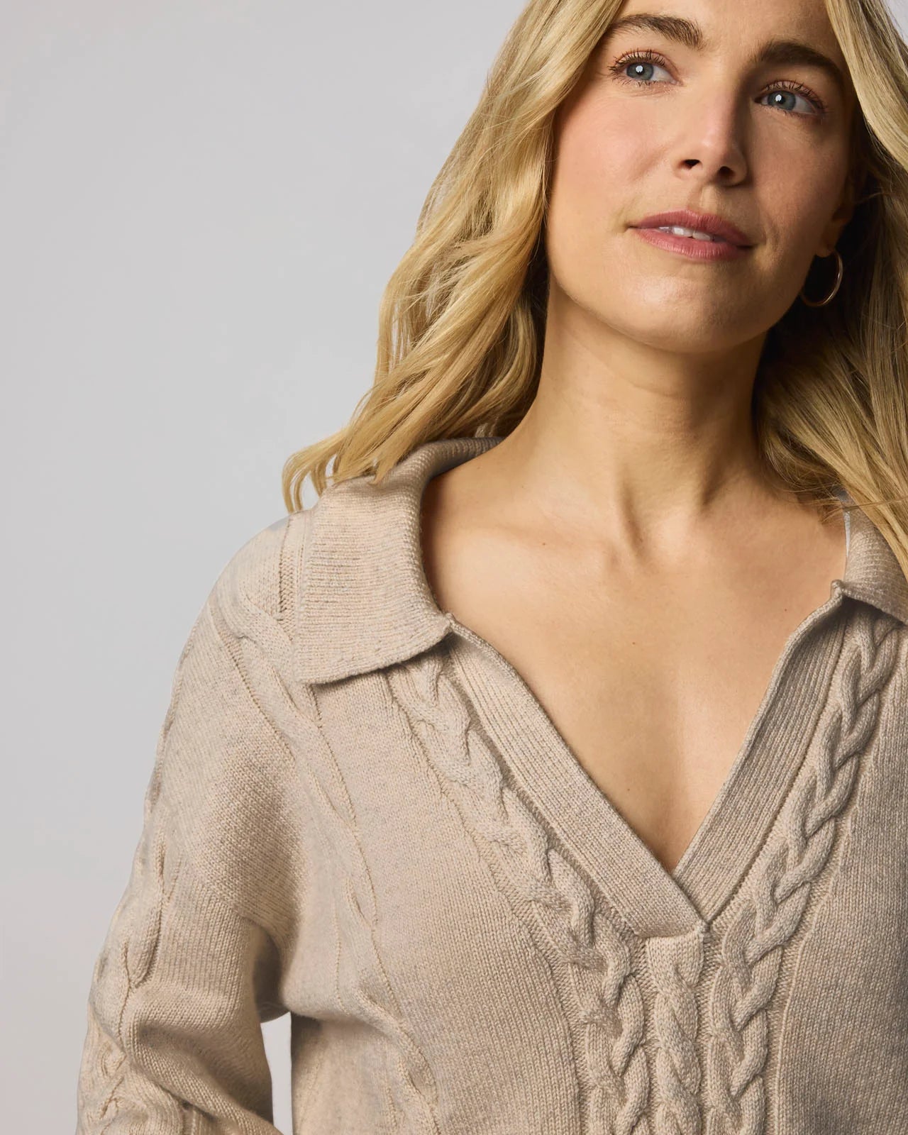 Woman wearing a beige cable knit sweater against a plain background