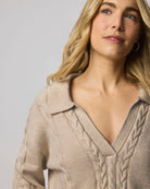 Woman wearing a beige cable knit sweater against a plain background