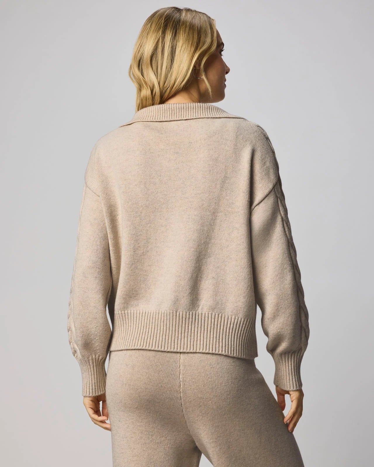 Person wearing a beige sweater and pants set against a plain background