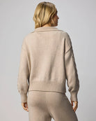 Person wearing a beige sweater and pants set against a plain background