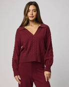 Woman wearing a burgundy sweater and pants against a plain background