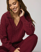 Woman wearing a burgundy cable knit sweater and pants against a plain background