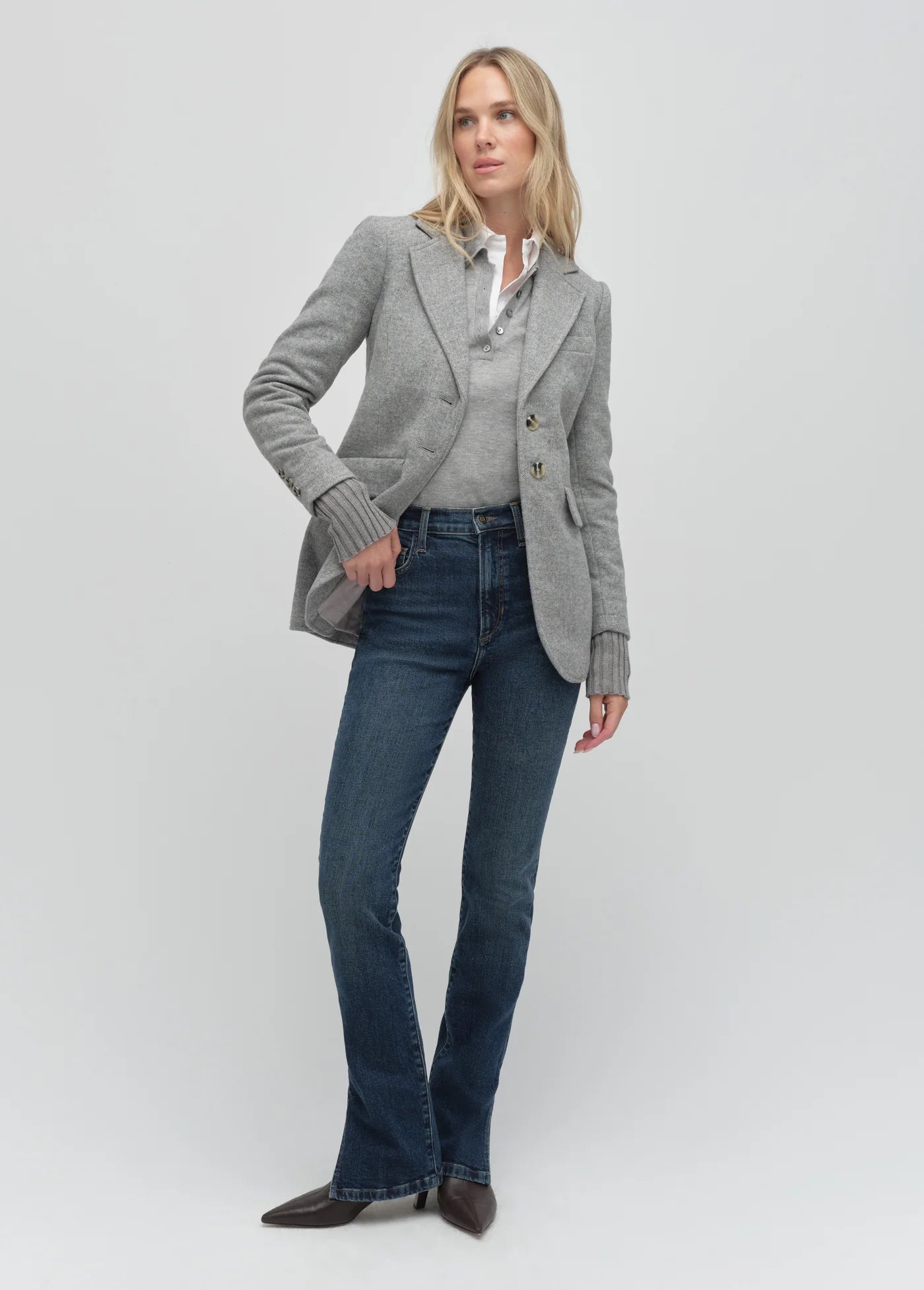 Woman wearing a gray blazer, white shirt, and blue jeans on a light gray background