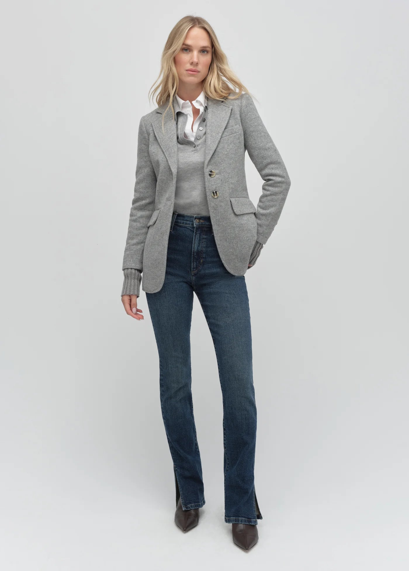 Woman wearing a gray blazer, white shirt, and blue jeans on a light gray background