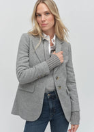 Woman wearing a gray blazer over a white shirt and blue jeans on a light gray background