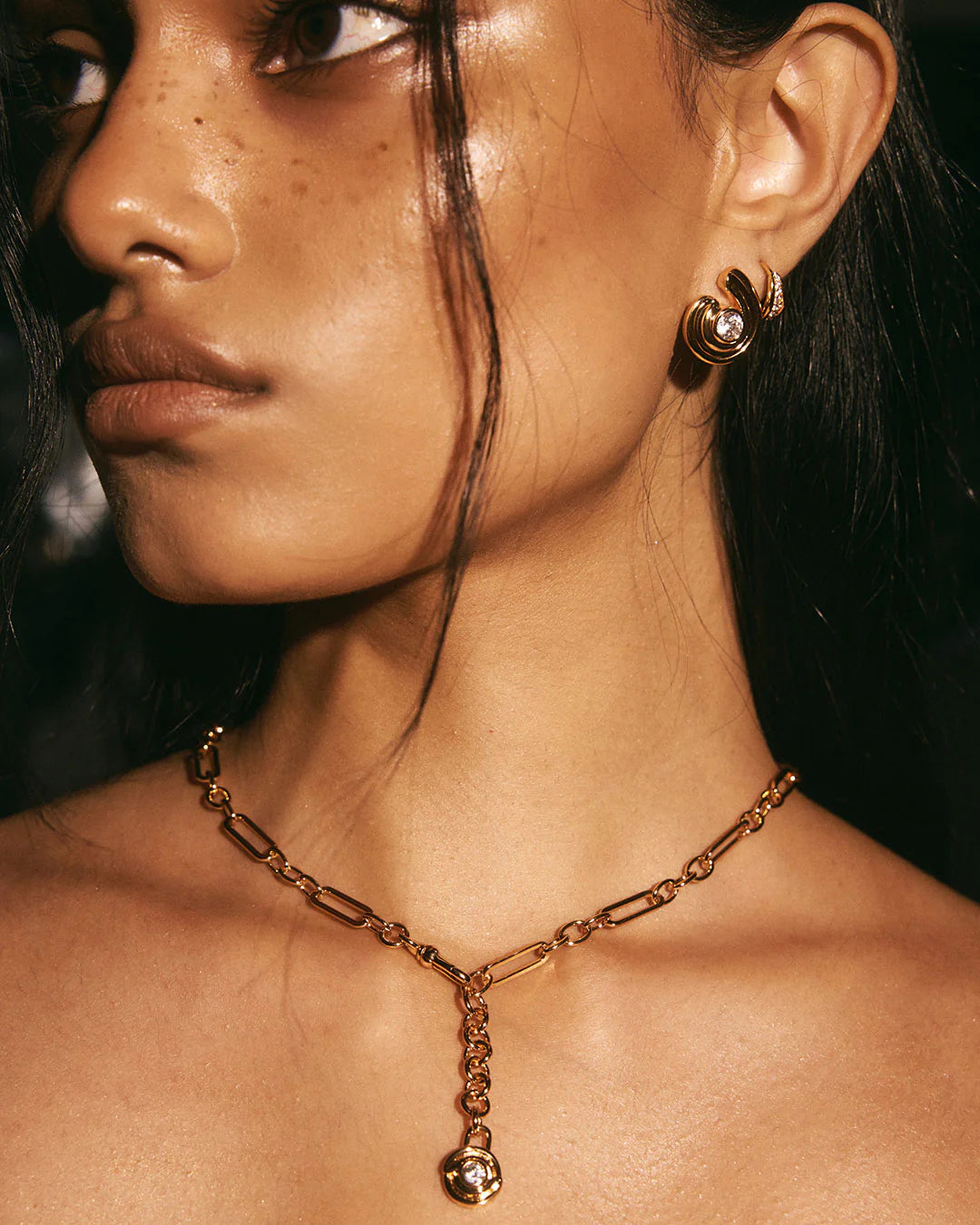 Close-up of a person wearing gold jewelry including earrings and a necklace.