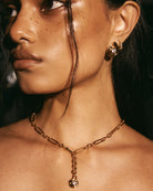 Close-up of a person wearing gold jewelry including earrings and a necklace.
